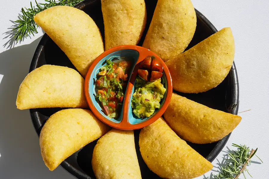 Des empanadas disposées en fleur dans une cazuela noire, autour de deux sauces