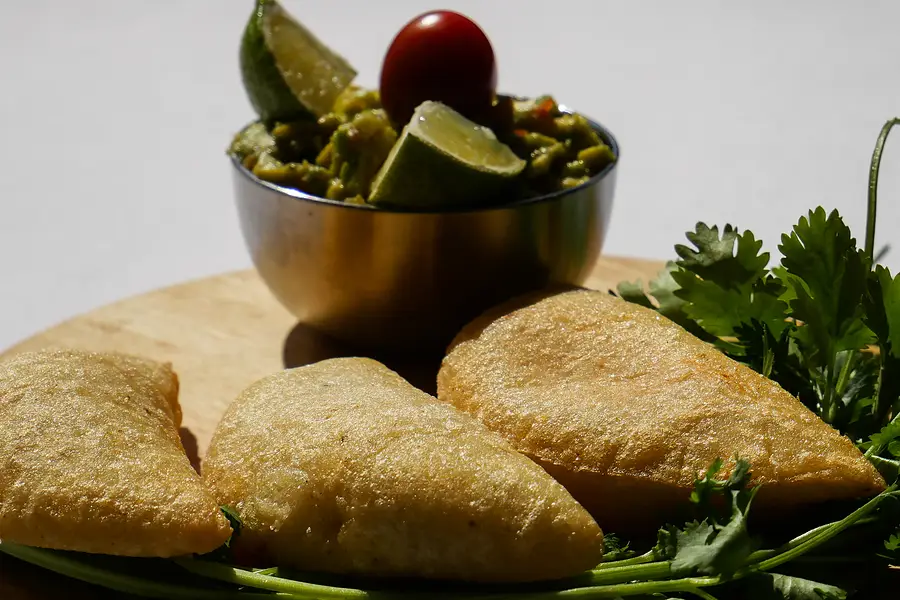 Des empanadas dorées sur une planche en bois, à côté d'un pot de guacamole