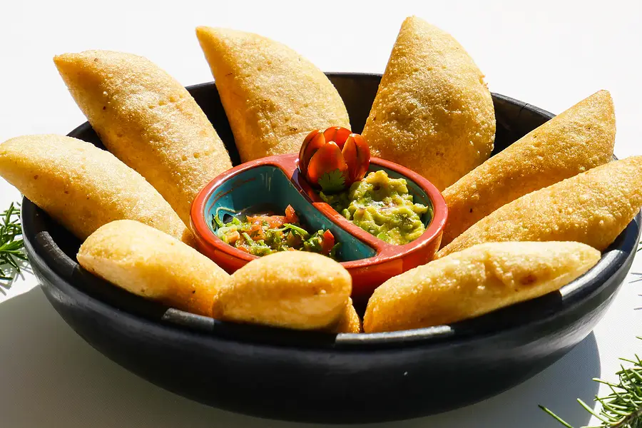 Des empanadas rangées dans une cazuela noire autour de deux sauces