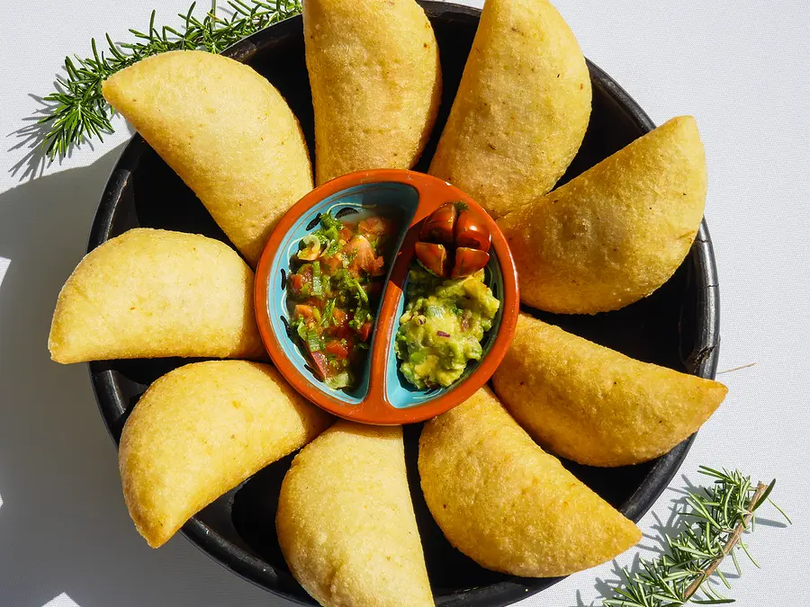 Des empanadas dorées disposées en fleur dans une cazuela noire, autour de deux sauces